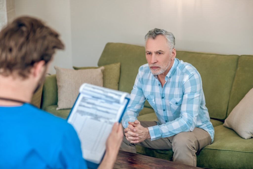 sad serious mature man dressed plaid shirt sitting sofa before dark haired doctor