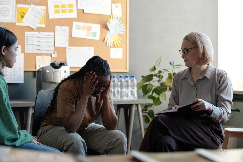 Distressed woman holding her head in group session while therapist listens and takes notes.